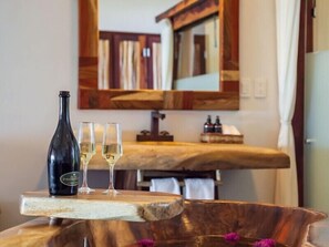 A wooden table with a bottle and glasses of white wine, a mirror, and a wooden countertop in a room.