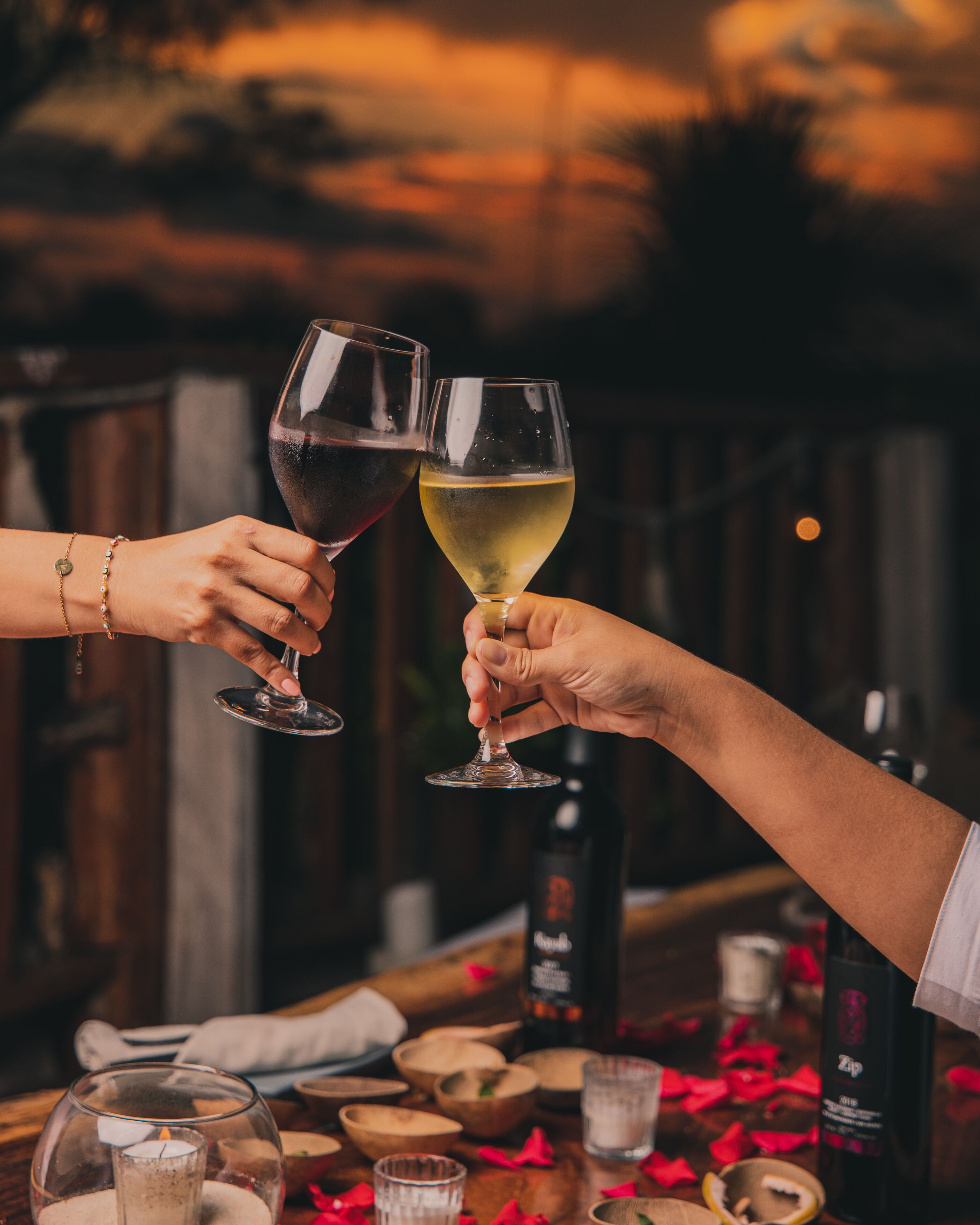 Two people toasting with wine glasses, a candle, and a bottle of wine on a table.