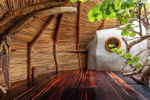 A room with a thatched roof, wooden beams, a potted plant, and a concrete block.