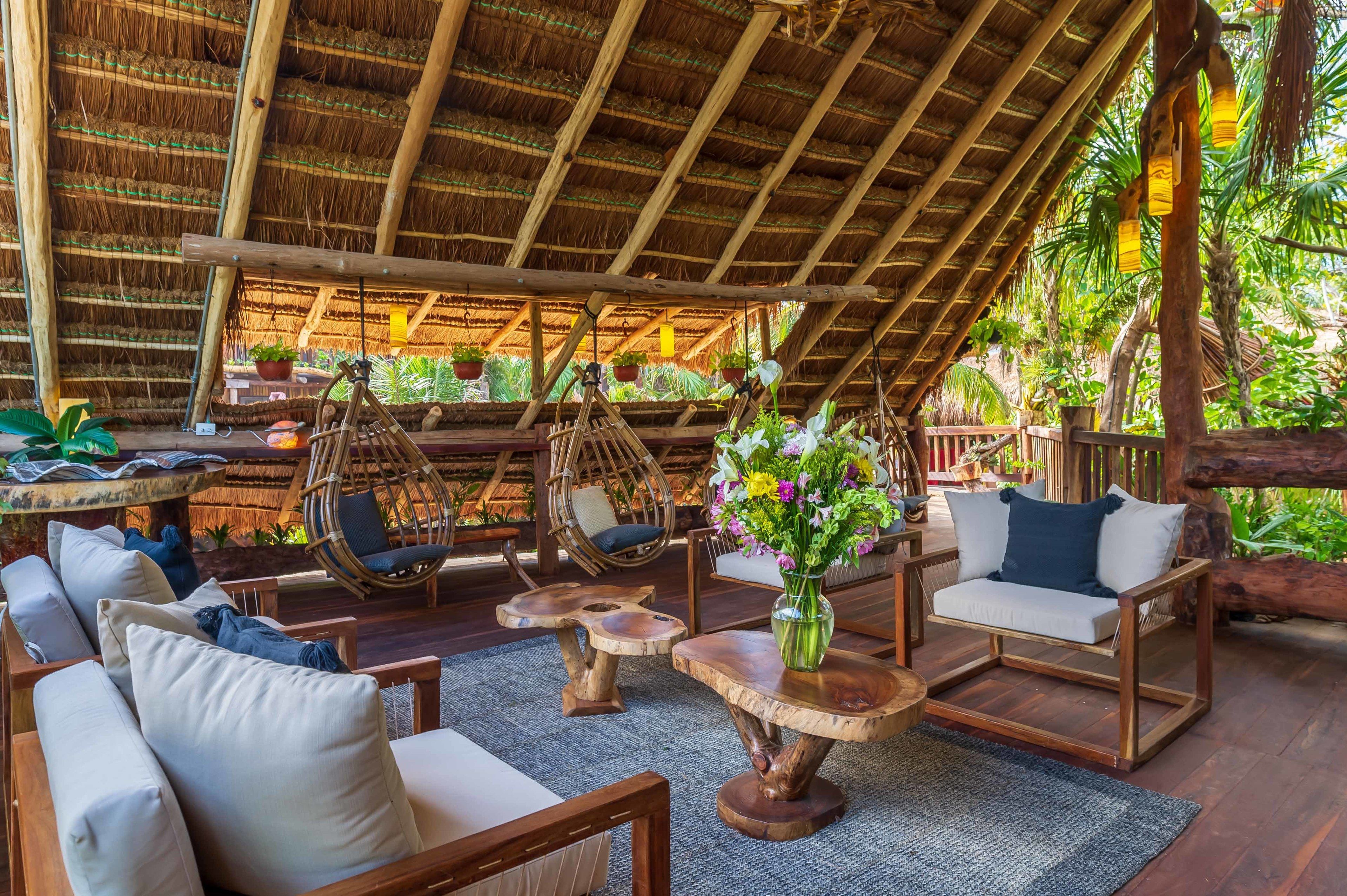 A thatched-roof outdoor seating area with wicker chairs and tables, surrounded by lush greenery.