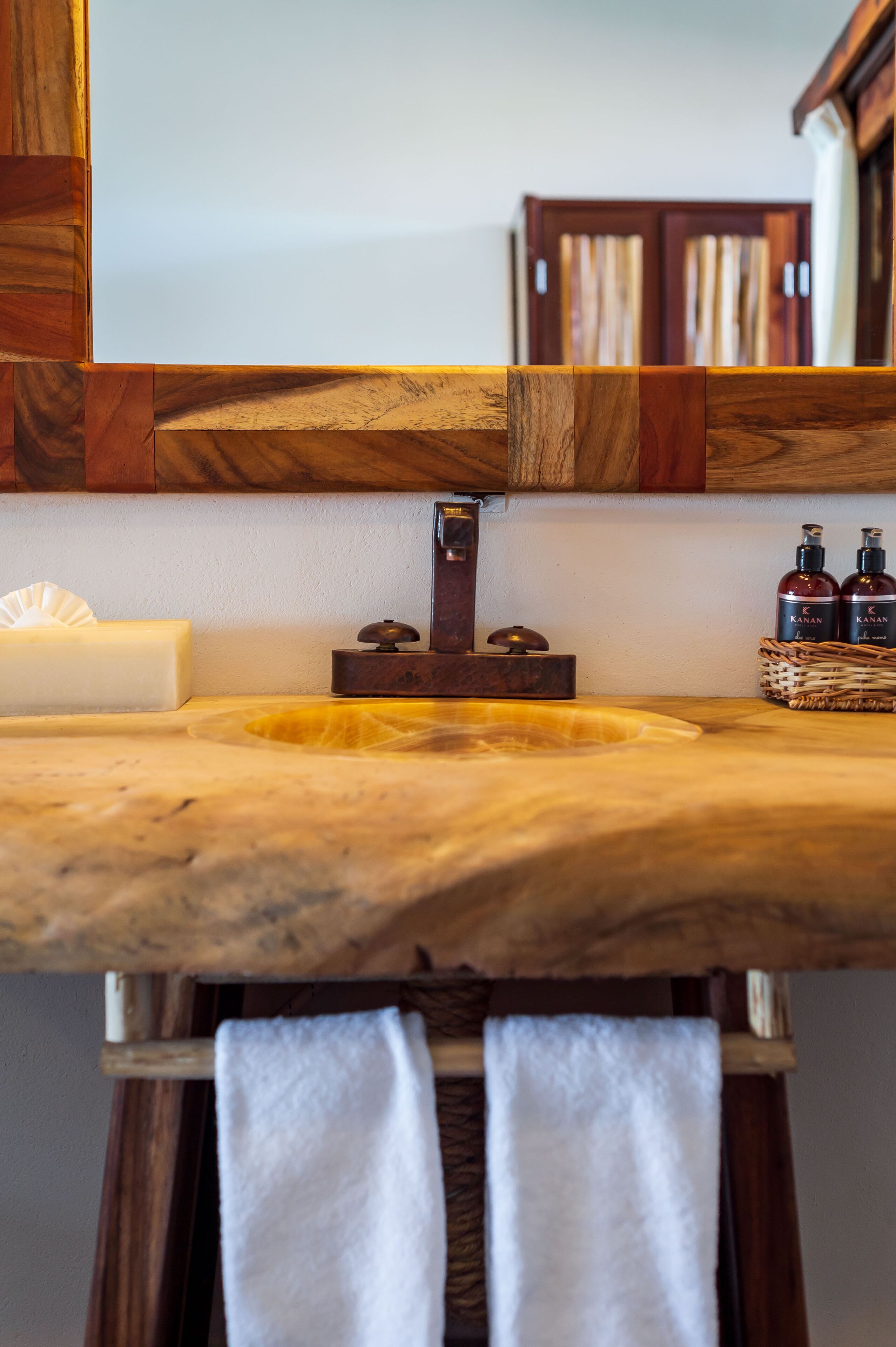 A wooden vanity with a marble countertop, a mirror, a soap dish, and two bottles of hand soap.