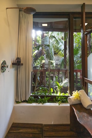 A bathroom with a bathtub, a shower curtain, a towel, and a window with a view of greenery.