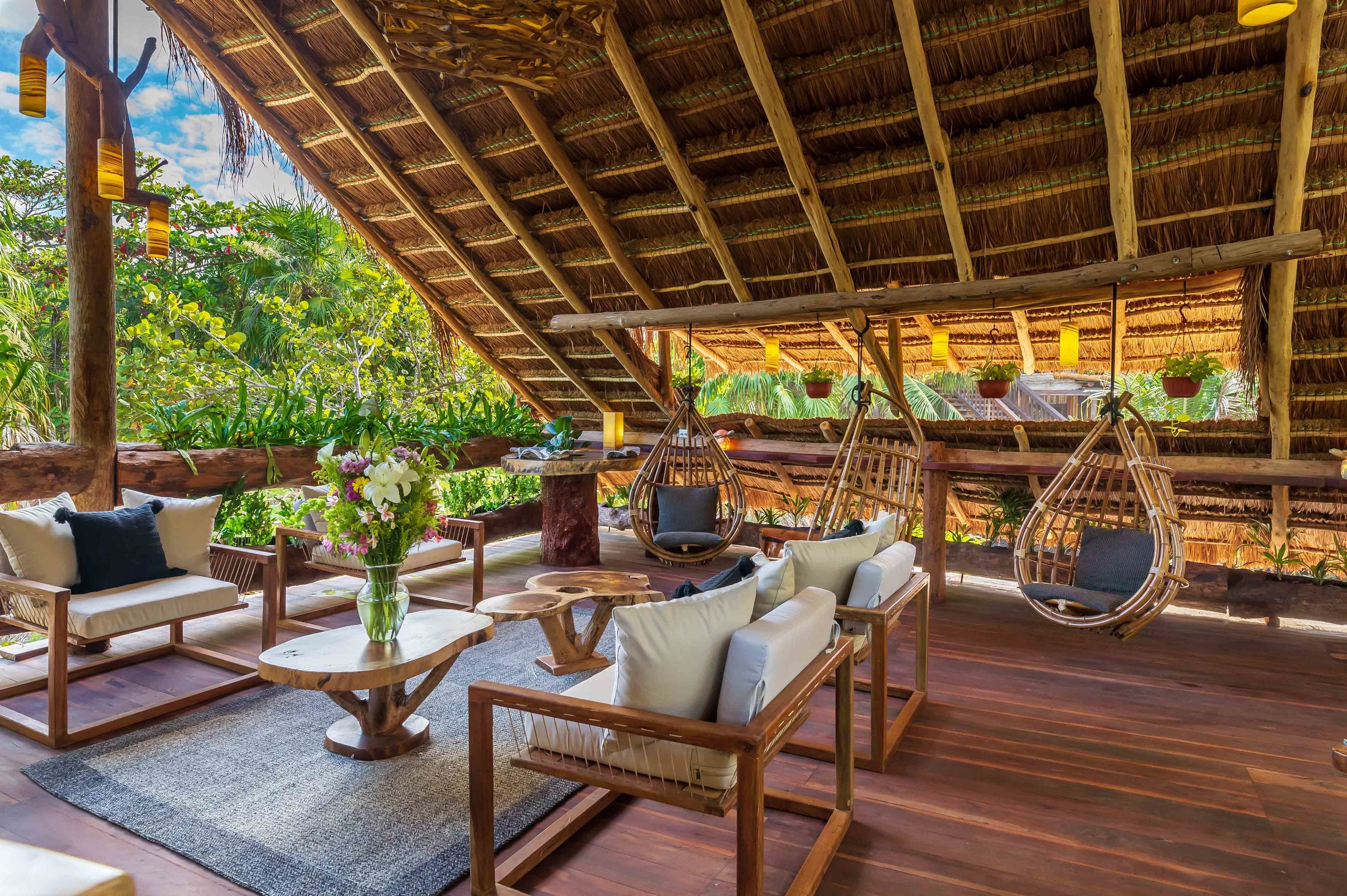 Una terraza de madera con mobiliario de mimbre, sillas colgantes y plantas en macetas.