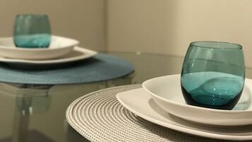 A dining table with a glass top, white plates, and a woven placemat.
