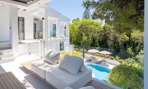 Un'area relax esterna moderna con piscina, mobili bianchi e vegetazione lussureggiante.
