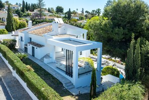 A modern white building with a rooftop terrace, a swimming pool, and a well-maintained garden.