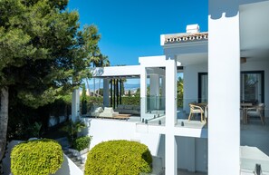 A modern house with a glass balcony, white exterior, and a view of the landscape.