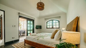 Quarto com cama, luminária de cabeceira, televisão e vista para o exterior pela janela.