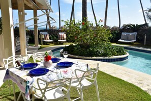 Un espace extérieur aménagé pour les repas, avec une piscine, des chaises blanches et des assiettes bleues.
