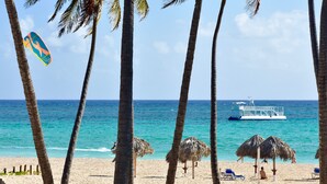 Uma praia com palmeiras, guarda-sóis de palha e um barco na água.