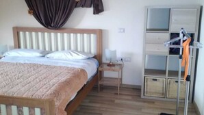 A bedroom with a wooden bed, a nightstand, a lamp, a wardrobe, and a vacuum cleaner. - Superb Mansarda ... (Caserta)