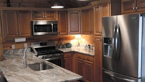 A kitchen with wooden cabinets, a stainless steel refrigerator, a microwave, a stove, and pendant lighting. - Chestatee River Cabin (Dahlonega)