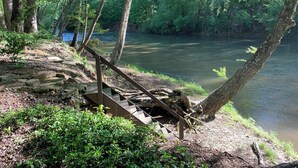 A wooden staircase leading down to a riverbank, surrounded by dense greenery and trees. - Chestatee River Cabin (Dahlonega)