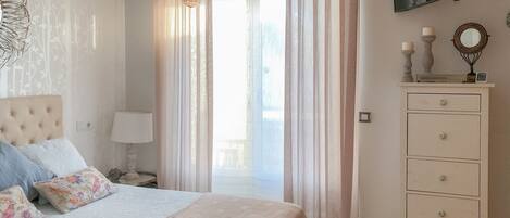 A bedroom with a bed, a nightstand, a dresser, and a window with sheer curtains.