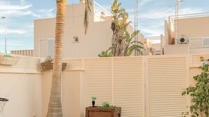 Un jardin à l’arrière d’une maison, avec un palmier, du gazon synthétique, un jardinier en bois et une clôture blanche.