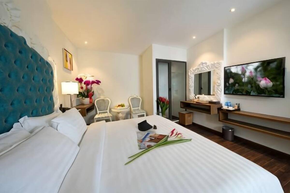 Een hotelkamer met een groot bed, een bureau met stoel, een kleine tafel, een spiegel en een televisie aan de muur.