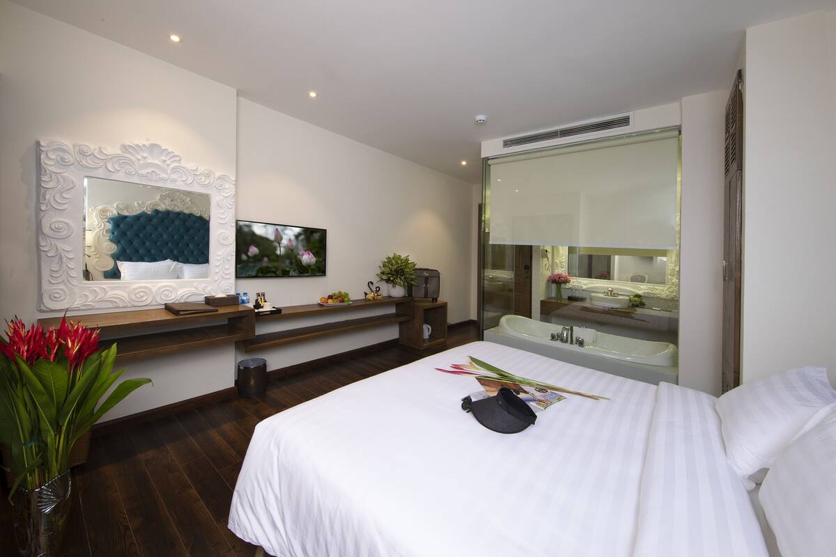 Een moderne hotelkamer met een groot bed, een kaptafel met spiegel, een televisie en uitzicht op de badkamer.