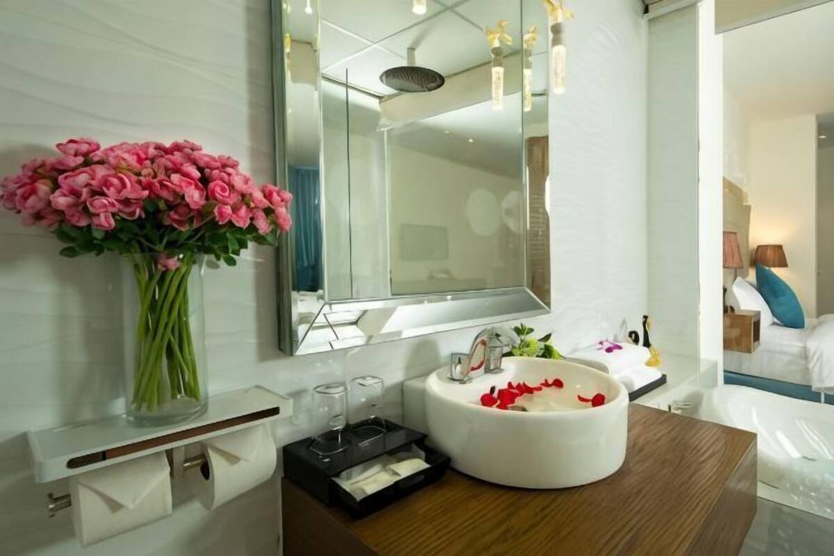 Een badkamer met een witte wastafel, spiegel en een vaas met roze bloemen.