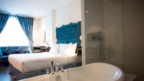 A hotel room with a large bathtub, a bed with white linens, a blue headboard, and a seating area with a blue sofa. - Diamond Hill Hotel (Ho Chi Minh City)