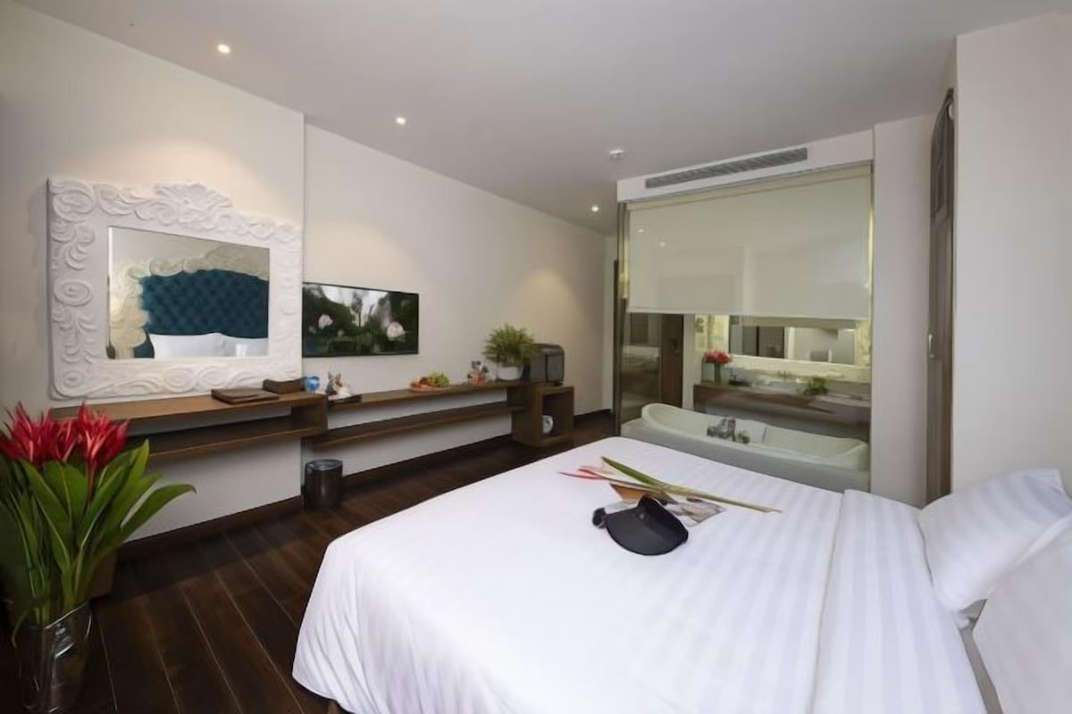 Un hotel moderno con una cama grande, una tocador con espejo, una pequeña mesa con objetos decorativos y vistas a la ciudad a través de la ventana.