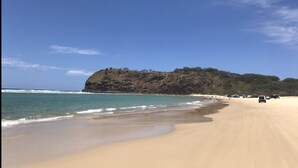 A beach with a sandy shore, a rocky hill in the background, and a clear blue sky.