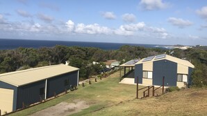 A coastal view with buildings, including a large warehouse and a residential structure with solar panels.