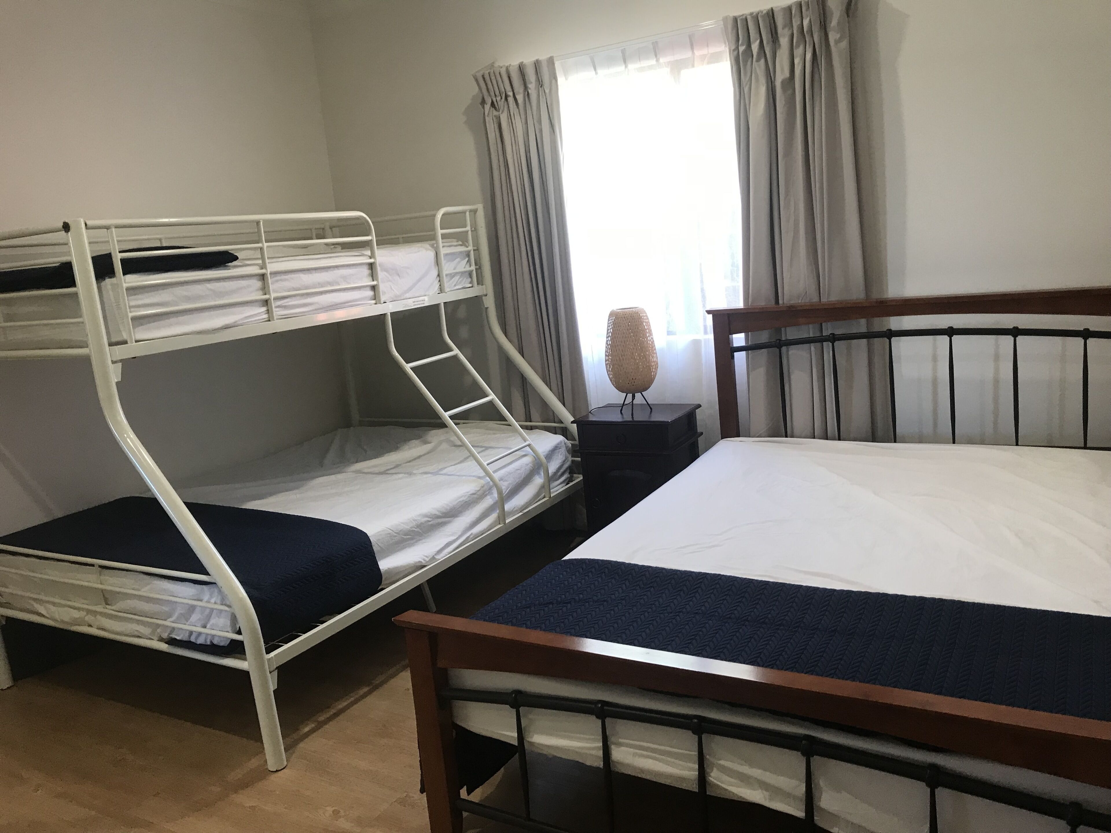 A room with two bunk beds, a single bed, a nightstand with a lamp, and a window with curtains.