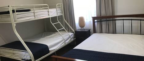 A room with two bunk beds, a single bed, a nightstand with a lamp, and a window with curtains.