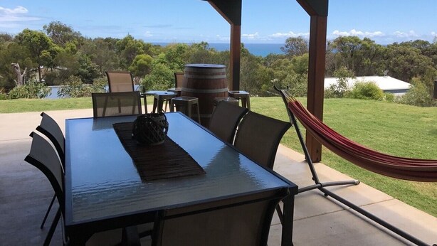 An outdoor patio with a table and chairs, a hammock, and a view of the ocean.