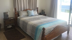 A bedroom with a wooden bed, a nightstand, a bedside table, and a window with curtains.