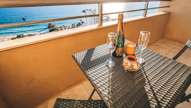A balcony with a table set for two, featuring a bottle of champagne, two glasses, and a candle holder.