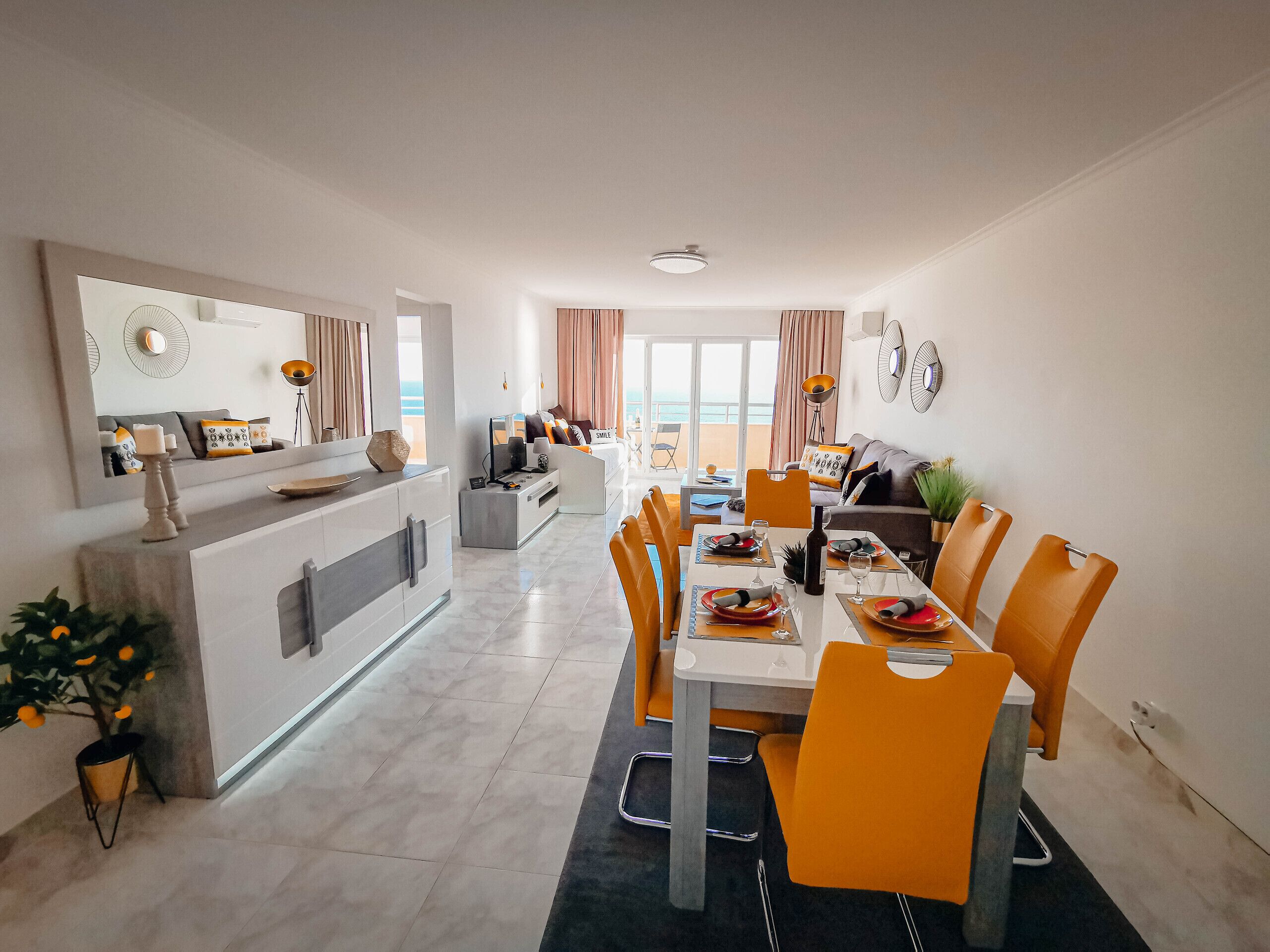 A modern dining area with a long table, orange chairs, and a central island with a sink and counter.