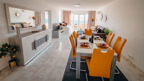 A modern dining area with a long table, orange chairs, and a central island with a sink and counter.