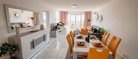 A modern dining area with a long table, orange chairs, and a central island with a sink and counter.