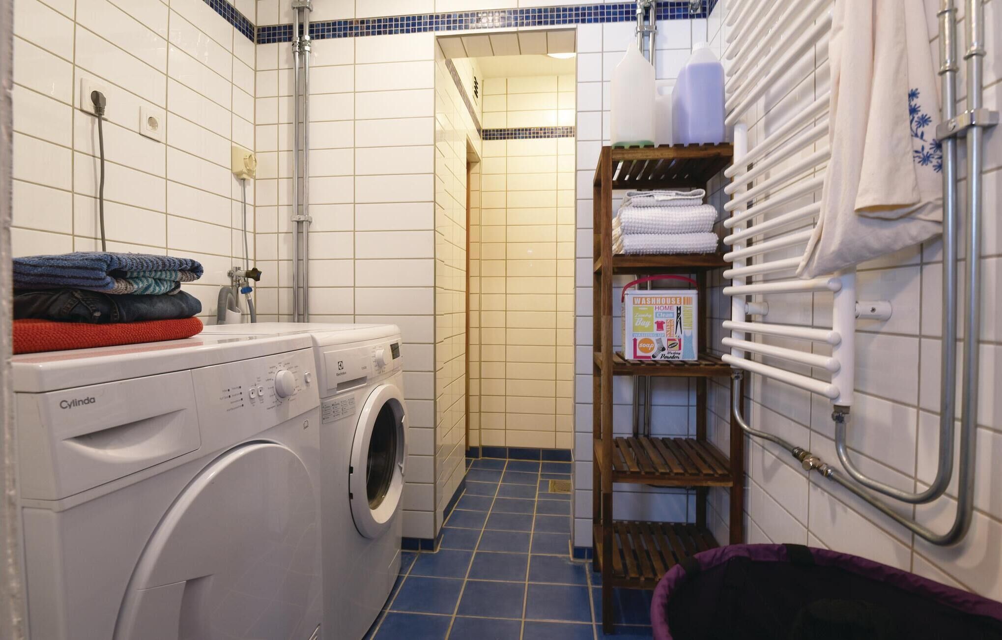 Un espace buanderie comprenant un lave-linge à chargement frontal, un étendoir et une étagère avec des serviettes pliées et du matériel de lessive.