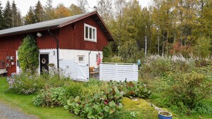 En rød lade med en hvid dør, omgivet af en have med forskellige planter og en blå potte.
