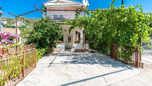 Eine Villa mit Fliesen-Terrasse, Satellitenschüssel und einem Garten mit Weinreben.