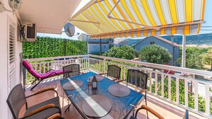 Ein Balkon mit einem Tisch für zwei Personen, Stühlen und einem gestreiften Sonnensegel.