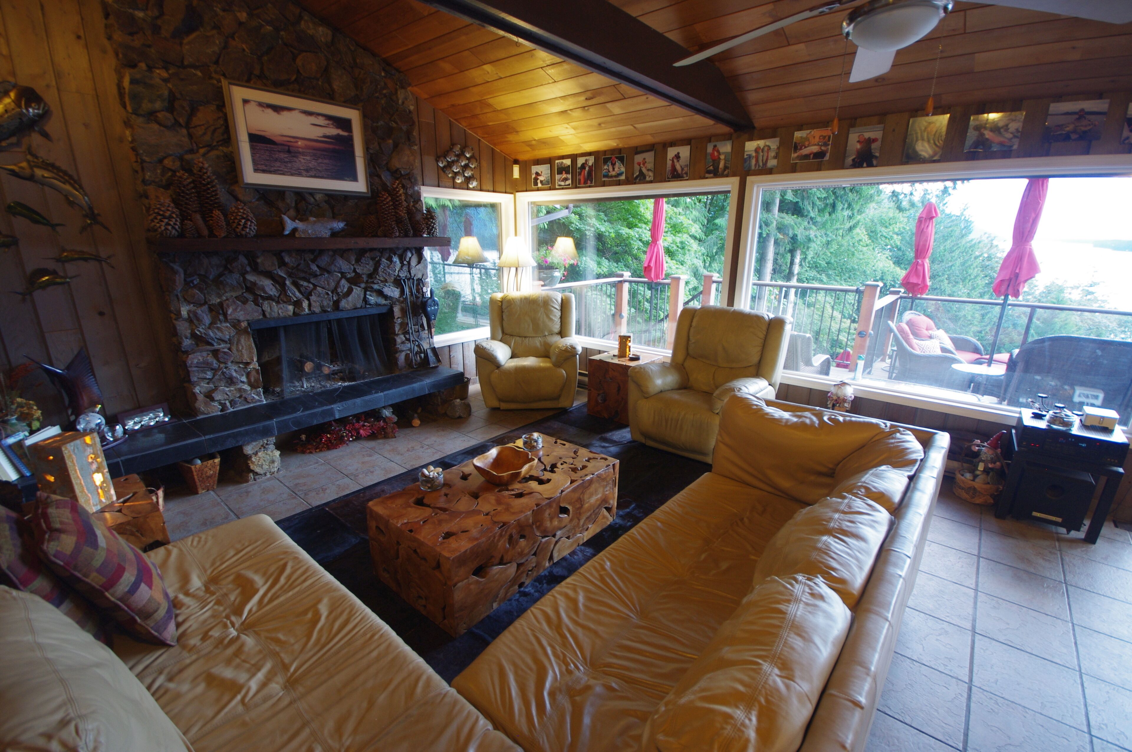 A cozy living room with a stone fireplace, comfortable seating, and large windows offering a view of the outdoors.