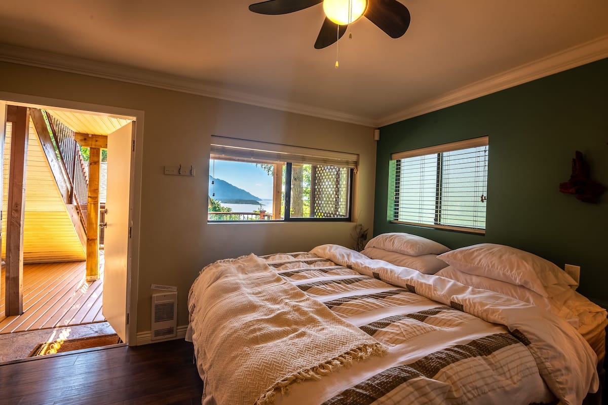 Un dormitorio con cama, dos ventanas, ventilador de techo y vistas al exterior.