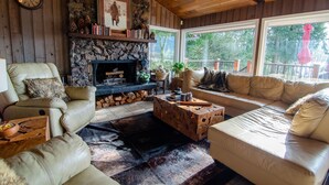 A cozy living room with a stone fireplace, leather sofas, and a large window offering a view of trees. - The Fraser River's Edge B&B Lodge (Chilliwack)