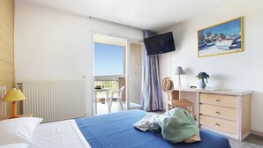 Habitación de hotel con cama, escritorio, silla, televisor y balcón con vistas.