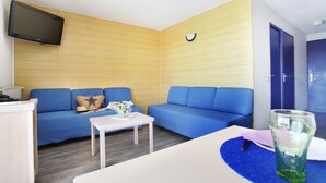 Un espacio habitable compacto con dos sofás azules, una mesita blanca, un televisor de pantalla plana montado en la pared y una puerta con manija.