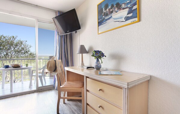 A room with a desk, chair, TV, lamp, vase, and a painting on the wall.