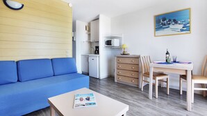 Un espacio habitable pequeño con un sofá azul, una pequeña mesa de comedor con sillas, una kitchenette y un cuadro en la pared.