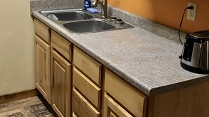 A kitchen with wooden cabinets, a granite countertop, a sink, and a coffee maker. - The Corral 2  room apartment next to The Yellowstone Rive (Gardiner)