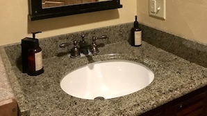A bathroom with a granite countertop, a white sink, a wooden mirror frame, and a wall-mounted light fixture. - The Corral 2  room apartment next to The Yellowstone Rive (Gardiner)