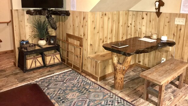 A cozy room with a wooden table, a bench, a TV mounted on the wall, and a patterned rug. - The Corral 2  room apartment next to The Yellowstone Rive (Gardiner)
