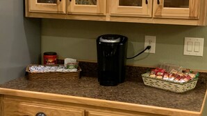A kitchen with wooden cabinets, a coffee maker, and a basket of snacks.