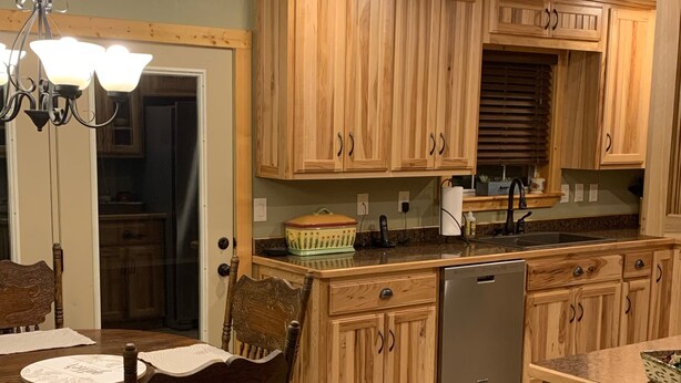 A kitchen with wooden cabinets, a dining table with chairs, a chandelier, and a dishwasher.